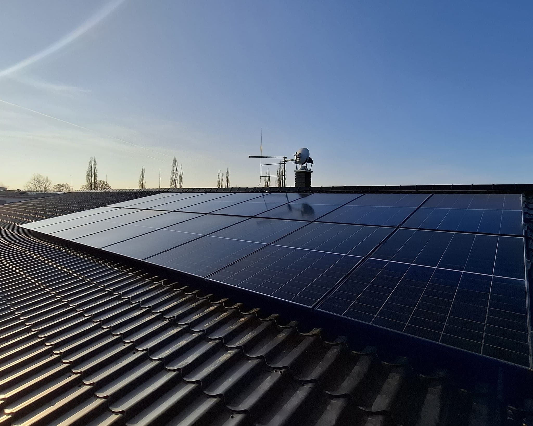 Fotovoltaické panely na tmavé taškové střeše rodinného domu, pohled podél řady panelů za soumraku, Blatná