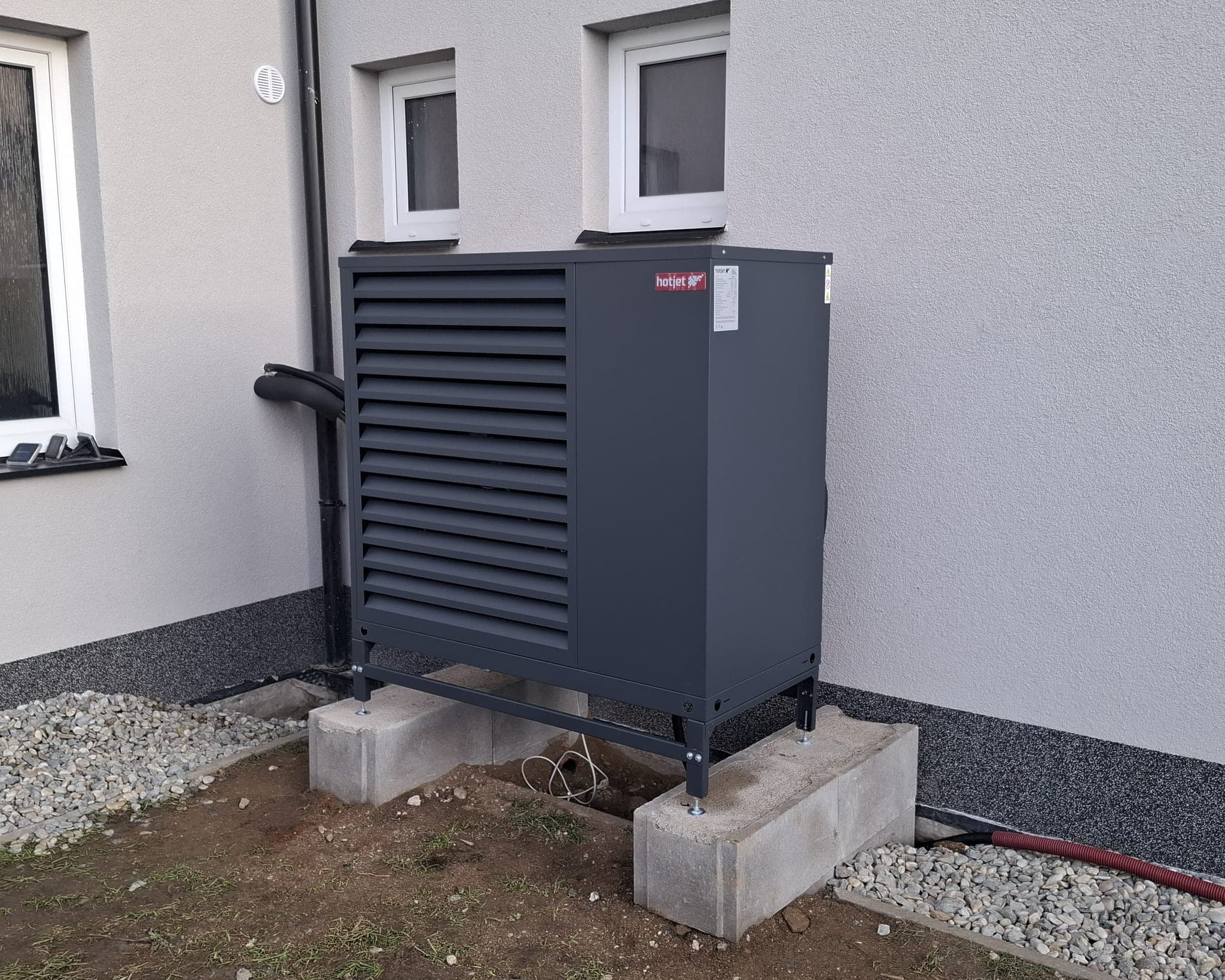Venkovní jednotka tepelného čerpadla HotJet postavená na betonových patkách u fasády rodinného domu, Blatná
