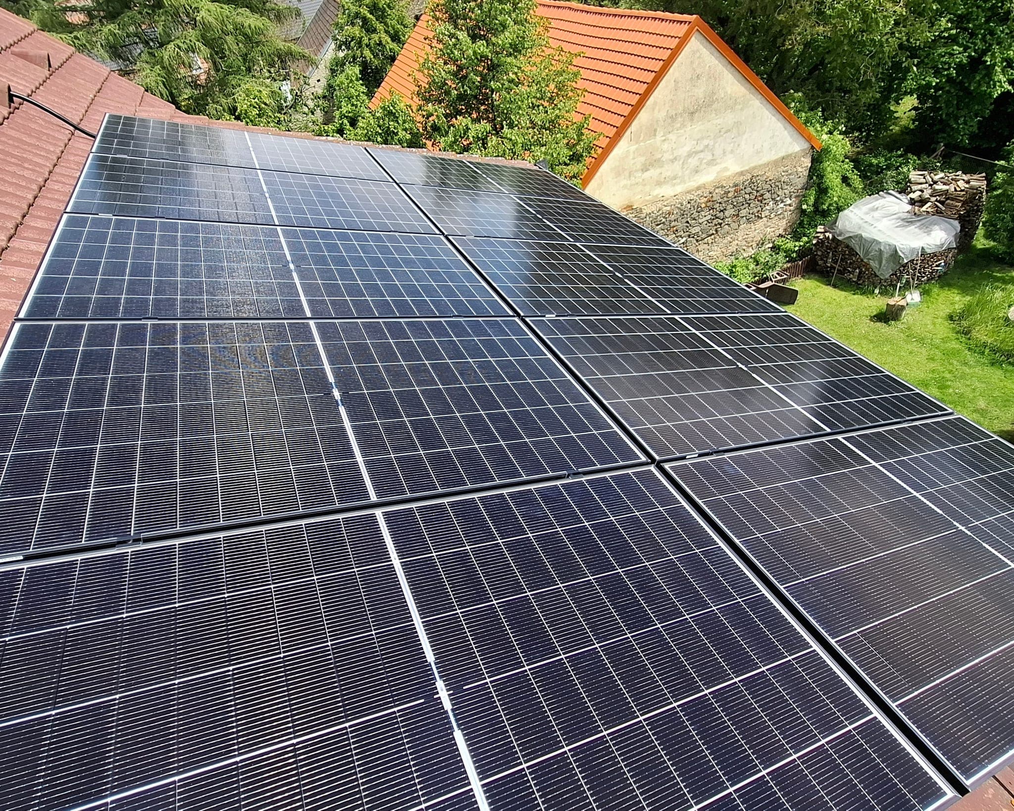 Detail černých fotovoltaických panelů na střeše rodinného domu, v pozadí zahrada a sousední stavení, Smetanova Lhota
