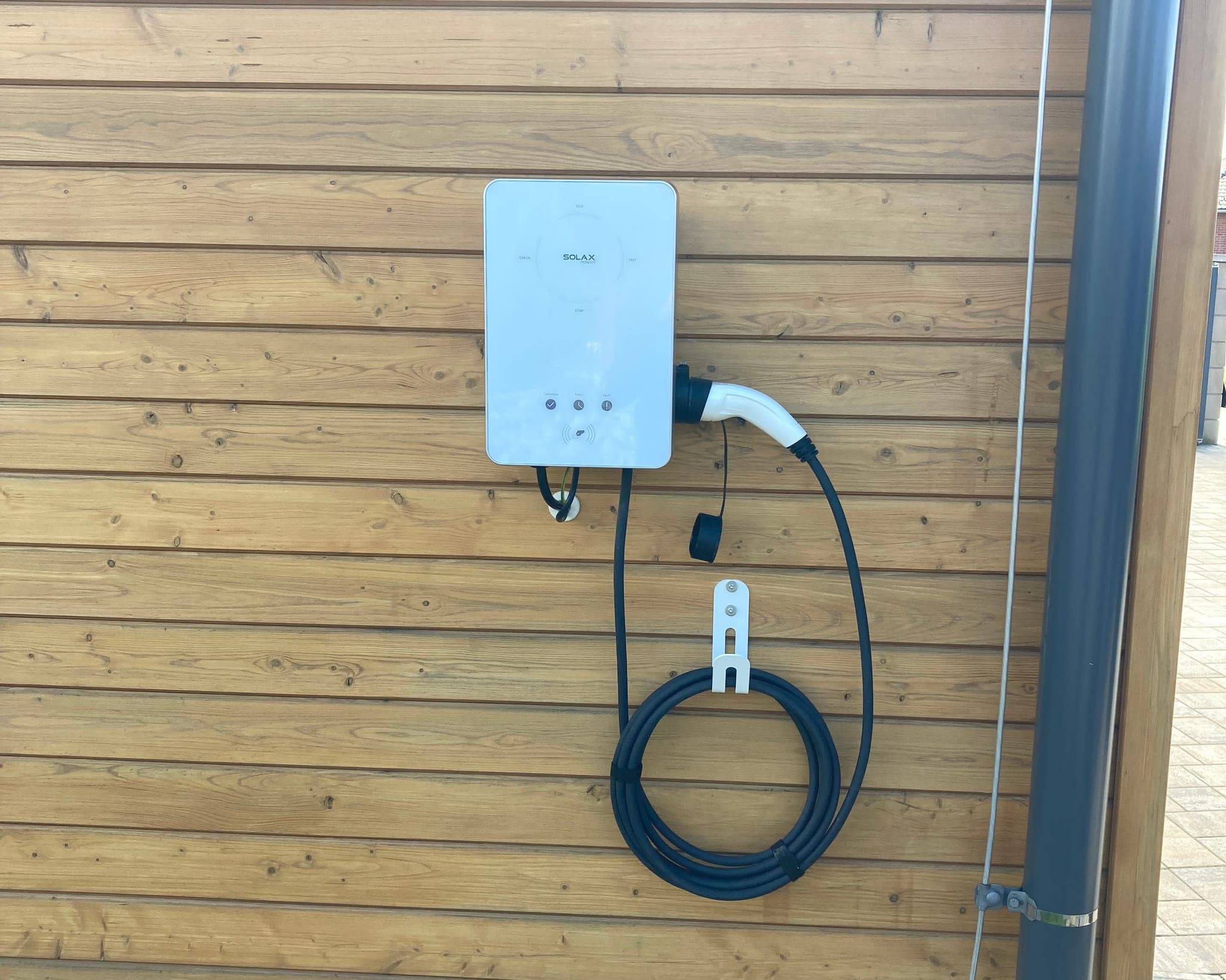 Světle modrá nabíjecí stanice wallbox Solax se zavěšeným nabíjecím kabelem na dřevěné stěně přístřešku, Blatná