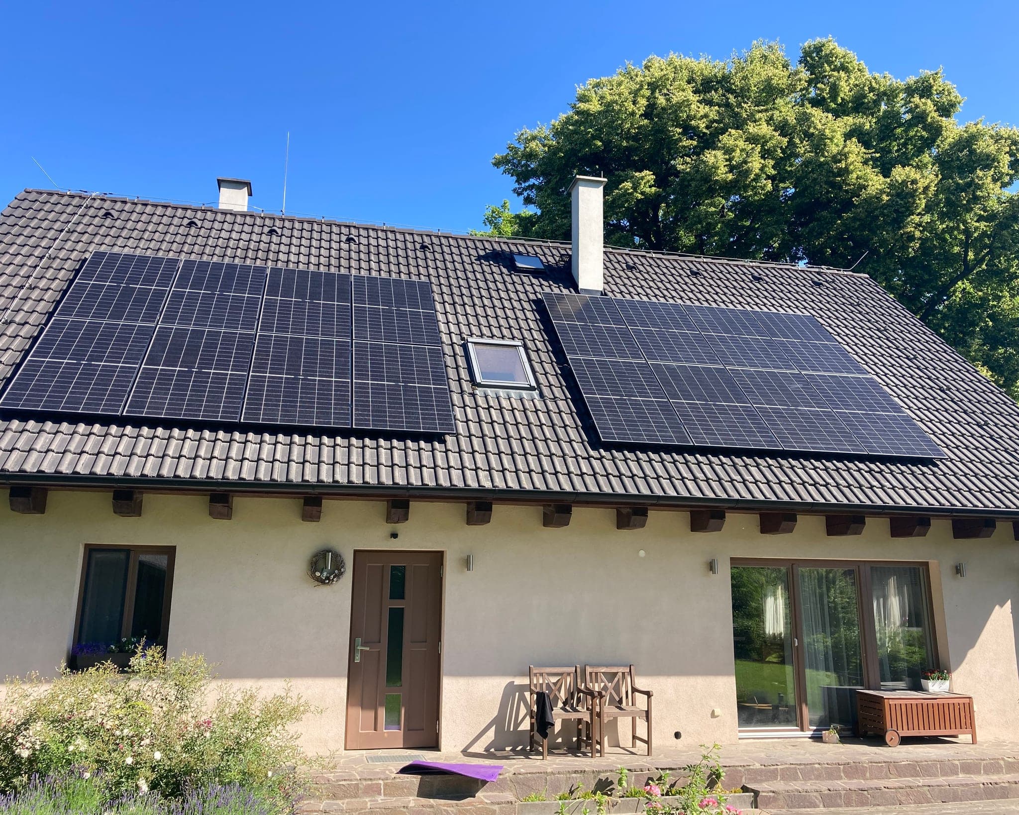 Dvě pole fotovoltaických panelů na tmavé střeše rodinného domu s dřevěným vstupním přístřeškem, Dmýštice
