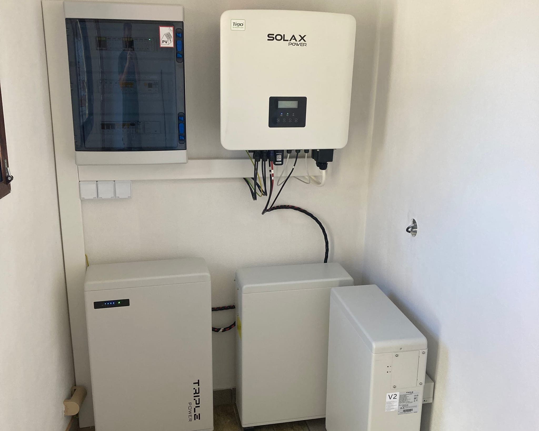 Nástěnný střídač SolaX a pod ním dvojice bateriových modulů v bílé technické místnosti, Rakovice